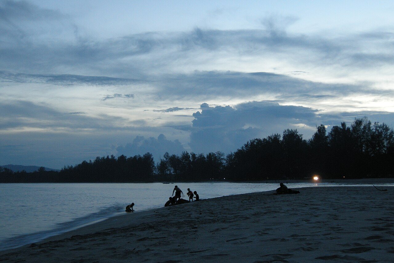 Cherating beach at dusk, the sky turning pink as people walk the sand after sunset